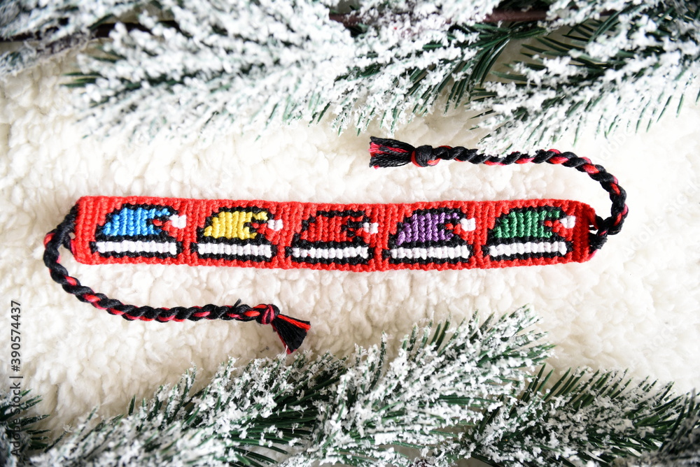 Woven friendship bracelet with bright alpha pattern Multicolored christmas  hats, handmade of thread, next to snowy fir branches. DIY Christmas or New  Year gift idea Photos | Adobe Stock