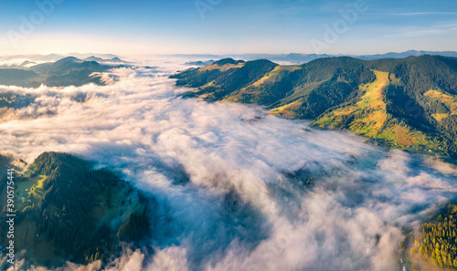 River of fog floving on the mountain valley. Sunny summer scene of Snidavka village. Amazing morning view from flying drone of Carpathian mountains, Ukraine, Europe..