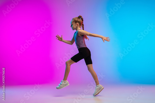 Active. Teenage girl, professional runner, jogger in action, motion isolated on gradient pink-blue background in neon light. Concept of sport, movement, energy and dynamic, healthy lifestyle.