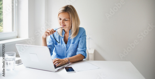 young and blond business woman with blue shirt and glasses is working in office and is happy