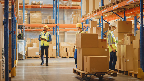 Canvas Print Handsome Male Worker Wearing Hard Hat Holding Digital Tablet Computer Walking Through Retail Warehouse full of Shelves with Goods
