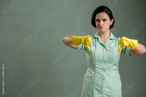 Young cleaning woman wearing a green shirt and yellow gloves showing double dislike © Cipri Suciu 
