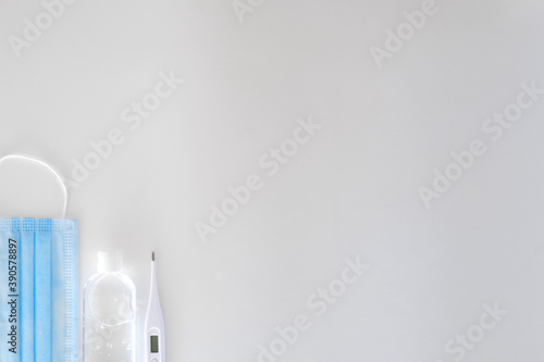 Fototapeta Naklejka Na Ścianę i Meble -  antiseptic in a transparent plastic bottle with a white cap white and white electronic thermometer lie on a light background next to a blue mask