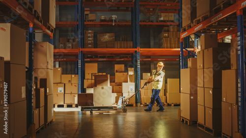 Photos Worker Moves Cardboard Boxes using Hand Pallet Truck, Walking between Rows of Shelves with Goods in Retail Warehouse