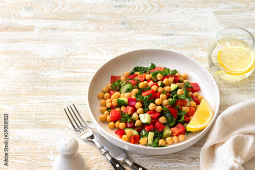 Healthy vegan salad with chickpeas, tomatoes, cucumbers, bell peppers and kale on light wooden background, space	