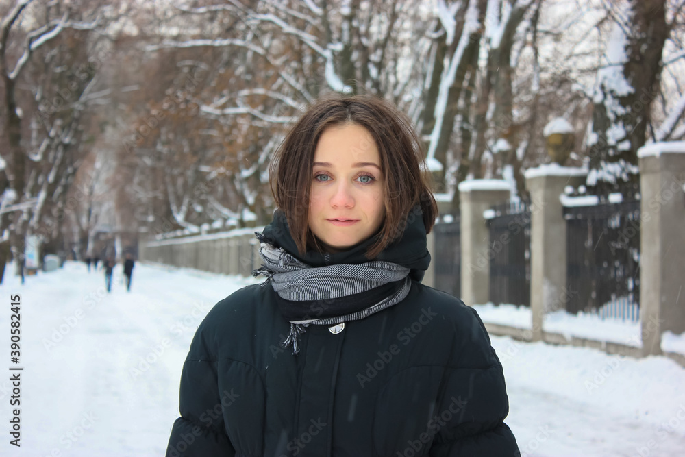 A young cute brunette girl with a bob hairstyle is smiling standing in a snowy park in winter. A young cute brunette girl with a bob hairstyle is smiling standing in a snowy park in winter.
