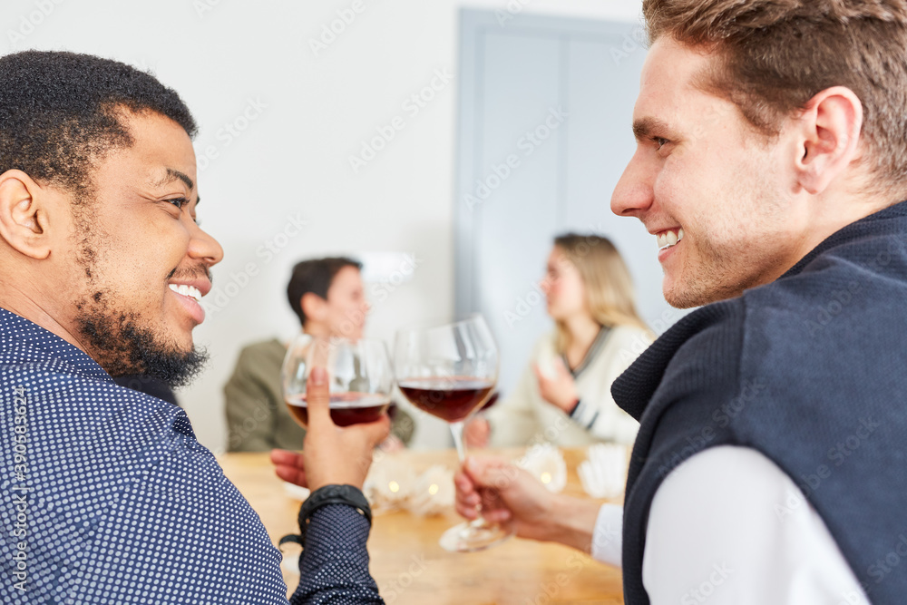 Zwei Männer stoßen mit Glas Wein auf Party miteinander an