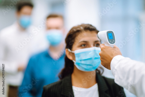 Body Temperature Control. Office staff  in protective face masks undergo temperature screening at the entrance. Epidemic virus outbreak concept. COVID-19.