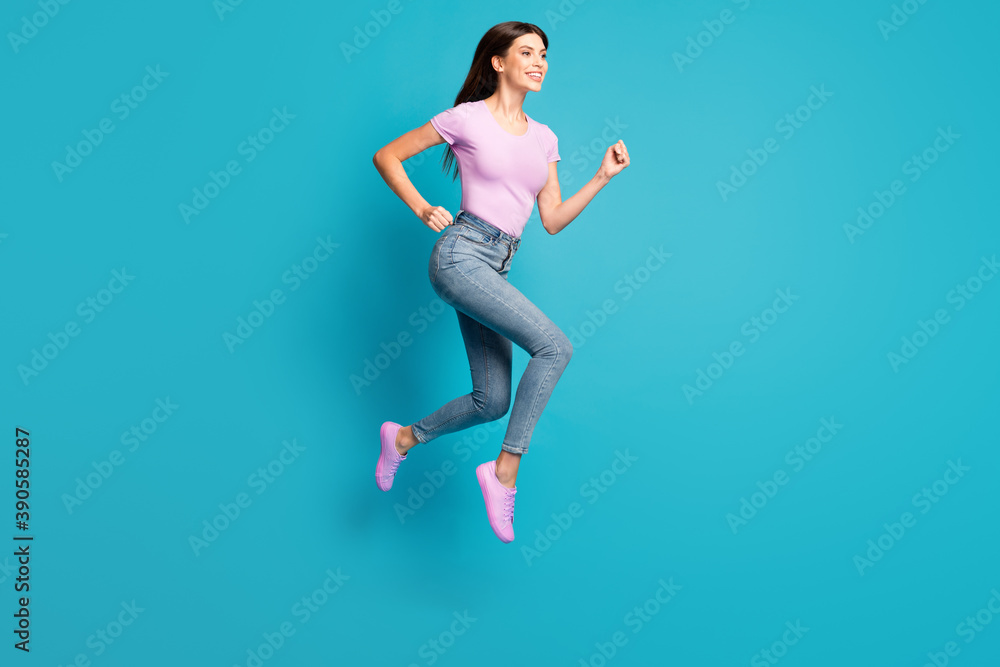 Full length profile photo of crazy young girl jump run wear pink t-shirt sneakers denim jeans isolated blue color background