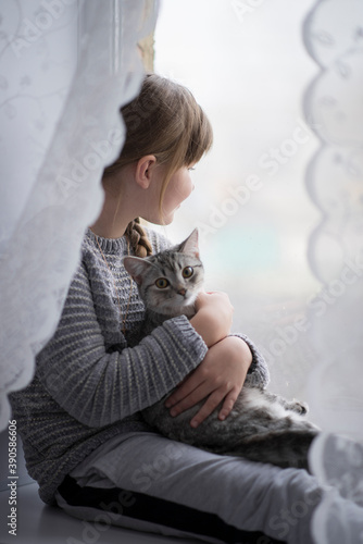 Fototapeta Naklejka Na Ścianę i Meble -  Portrait. A girl with long hair is sitting on the window with a cat.