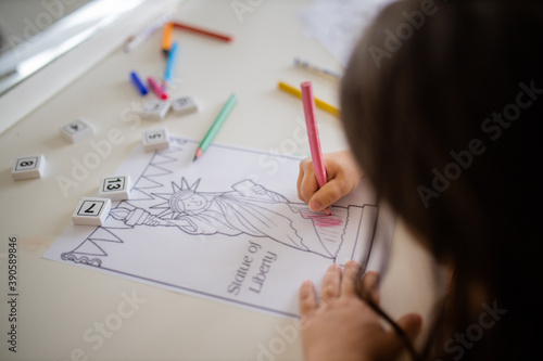 Little girl coloring an image of the Statue of Liberty with a pink pencil