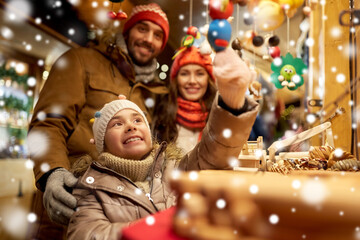 family, winter holidays and celebration concept - happy mother, father and little daughter choosing souvenirs at christmas market on town hall square in tallinn, estonia over snow