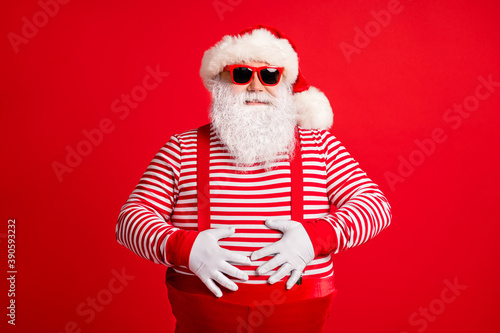 Portrait of his he nice handsome attractive cheerful cheery grey-haired Santa touching fat belly abdomen wearing gloves isolated over bright vivid shine vibrant red color background © deagreez