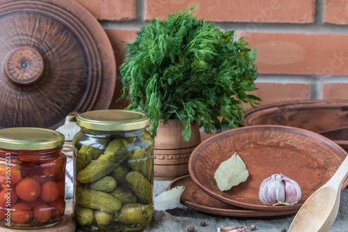 Canned tomatoes and cucumbers in jars with spices, garlic, pepper and dill on a brick wall background