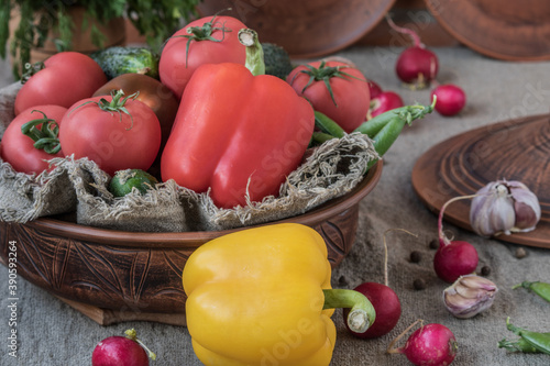 Bell pepper red and yellow, tomatoes, cucumbers, garlic, green peas, radish, dill in a clay bowl against a brick wall background