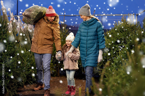 family, winter holidays and people concept - happy mother, father and little daughter buying christmas tree at street market in evening over snow photo