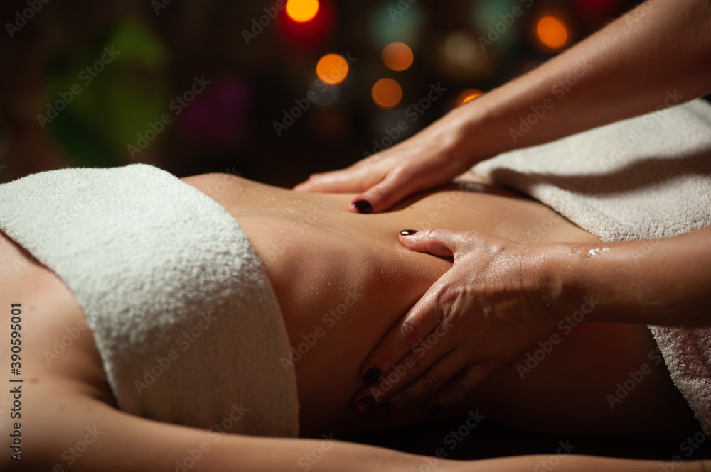 Fototapeta premium Close up of therapist doing stomach massage on woman in spa against dark background.