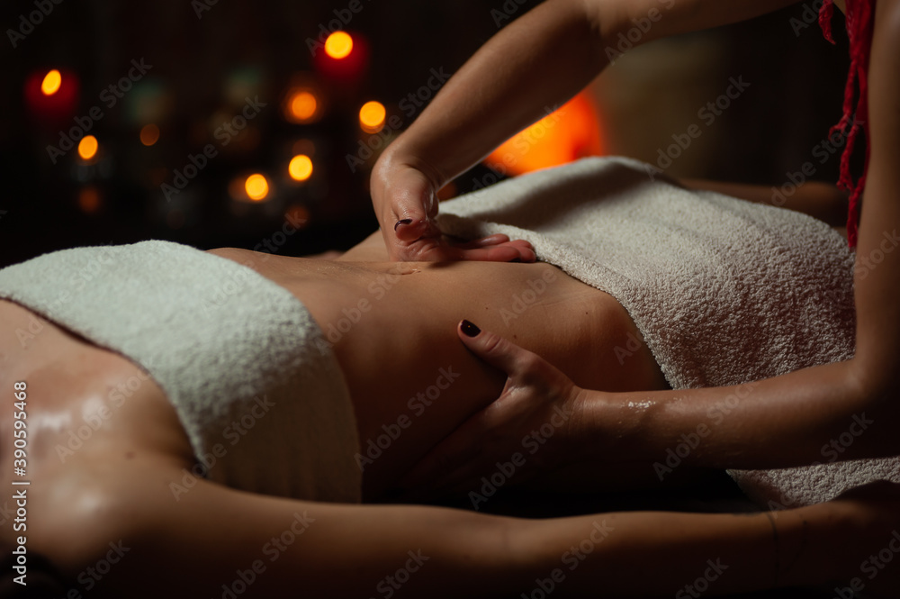Obraz premium Close up of therapist doing stomach massage on woman in spa against dark background.