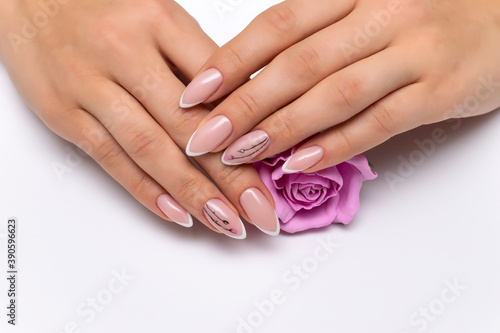 Extension of nails. Wedding french white manicure with painted flowers on sharp long nails holding a pink rose. Close-up on a white background.