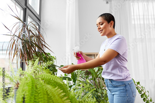 Obraz na plátně people, housekeeping and plants care concept - african american woman spraying h