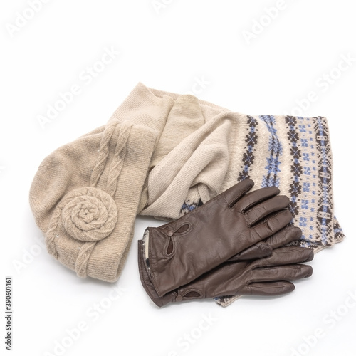 Women's accessories for winter and autumn. Knitted beige hat, warm scarf with an ornament. Brown gloves made of genuine leather with a fur lining. Isolated over white background.