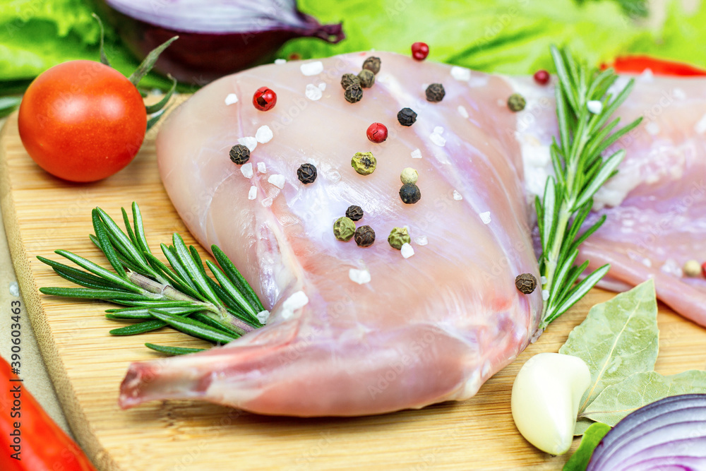 Raw uncooked pink rabbit leg meat with green rosemary and fresh vegetables on light wooden cutting board background. Raw uncooked pink rabbit leg meat with green rosemary and fresh vegetables on light wooden cutting board background.