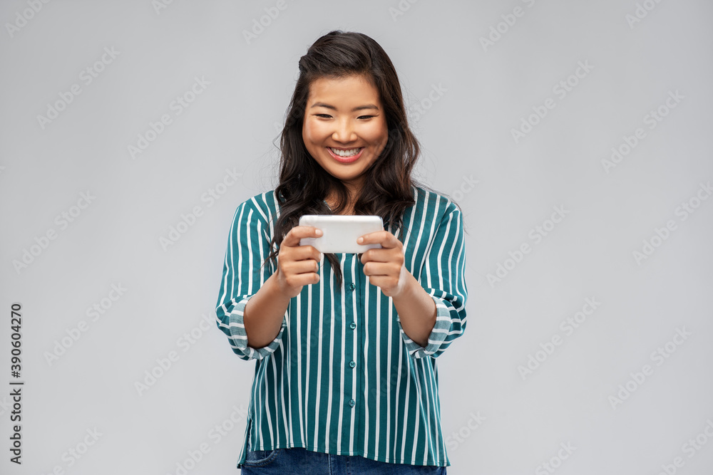 technology and people concept - happy asian woman using smartphone over grey background technology and people concept - happy asian woman using smartphone over grey background