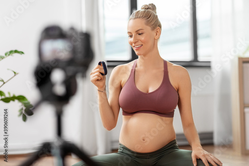 sport, yoga and media concept - happy pregnant woman or blogger with camera on tripod and fitness tracker ecording online yoga class at home © Syda Productions