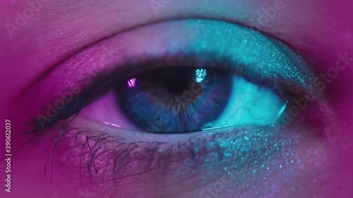 Close up shot of eye opening with blue iris. Healthy eyesight concept. Female blue eye in neon light. Young sexy girl in a nightclub. Macro look of the human eye. Pink-blue-green color, euphoria. photo