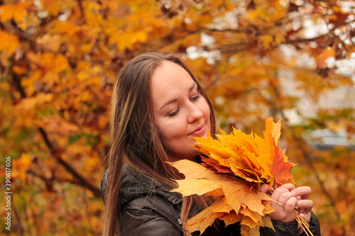 A smiling young woman holds yellow maple leaves in her hands. Happy young woman in autumn Park. A woman enthusiastically catches falling leaves. 