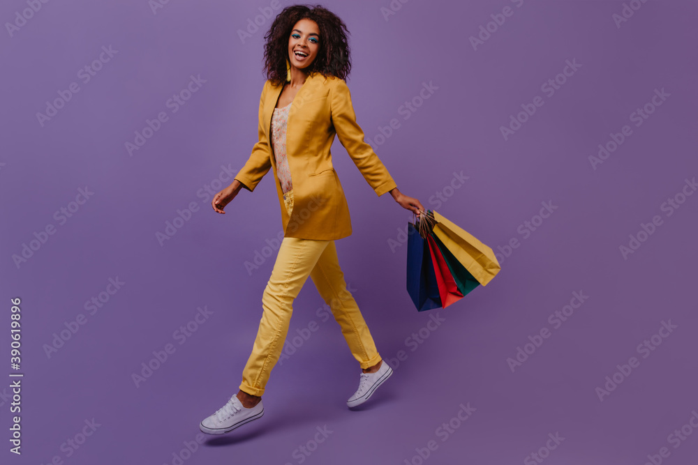 Full-length portrait of curly woman with store bags. Attractive black girl enjoying sales.