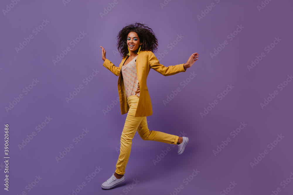 Appealing girl with wavy hair jumping in studio. Attractive african woman wears yellow costume dancing during photoshoot.