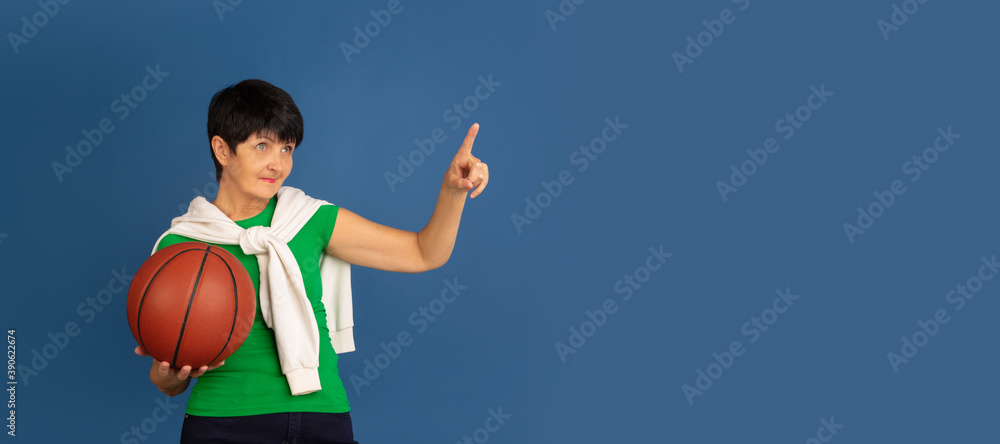 Playing basketball. Portrait of senior woman in stylish outfit isolated on blue studio background. Tech and joyful elderly lifestyle concept. Trendy colors, forever youth. Copyspace for ad. Flyer Playing basketball. Portrait of senior woman in stylish outfit isolated on blue studio background. Tech and joyful elderly lifestyle concept. Trendy colors, forever youth. Copyspace for ad. Flyer