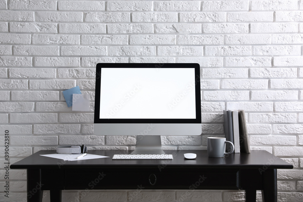 Fototapeta premium Comfortable workplace with modern computer on black table near white brick wall. Space for text