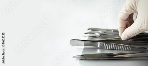 Template horizontal banner with surgical instruments on a white background, space for text. Gloved hand takes tools. Medical clamp, scalpel, needle holder.