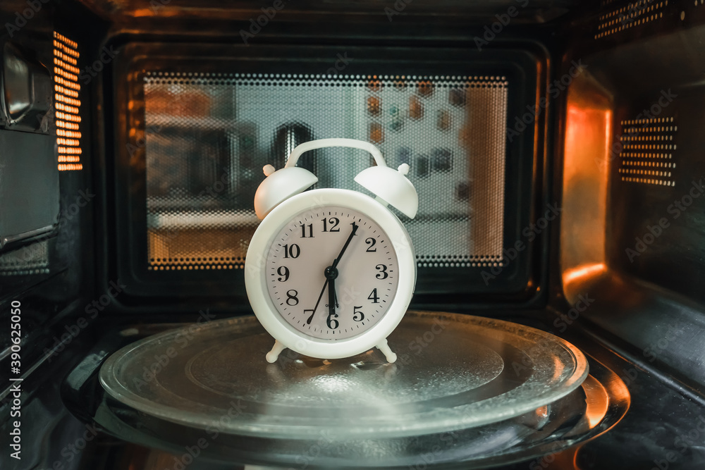 White alarm clock for 6 am is inside the microwave, photo from the
