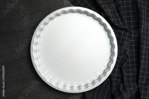 Baking dish and tablecloth on black table, flat lay. Cooking utensil