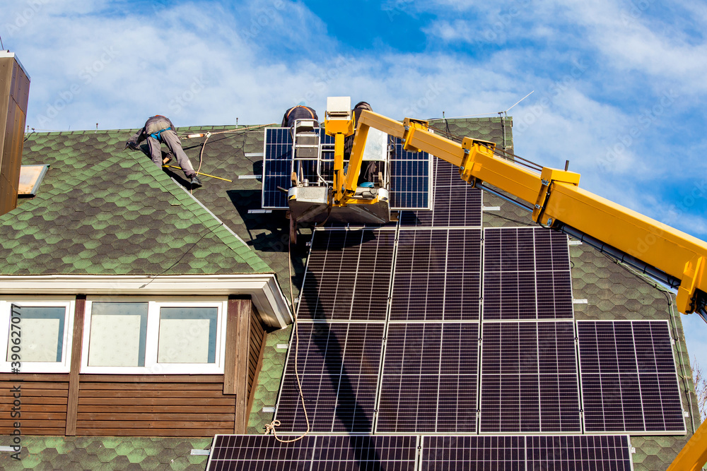 Fototapeta premium Workers installing solar panels on private home hexagonal roof felt on sunny day, blue sky. Real life. Home power plant.