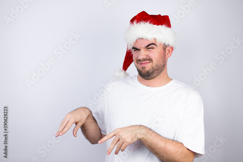 Quadro su tela Young handsome man wearing a Santa hat over white background disgusted expression, displeased and fearful doing disgust face because aversion reaction