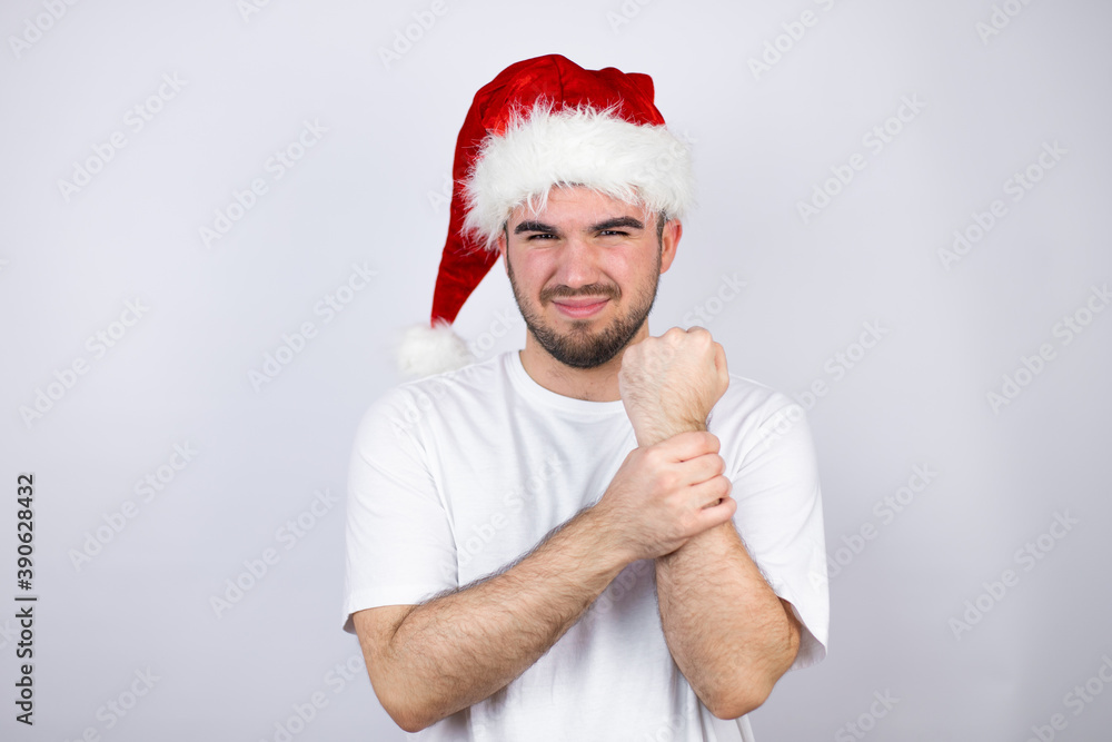 Young handsome man wearing a Santa hat over white background suffering pain on hands and fingers, arthritis inflammation Young handsome man wearing a Santa hat over white background suffering pain on hands and fingers, arthritis inflammation