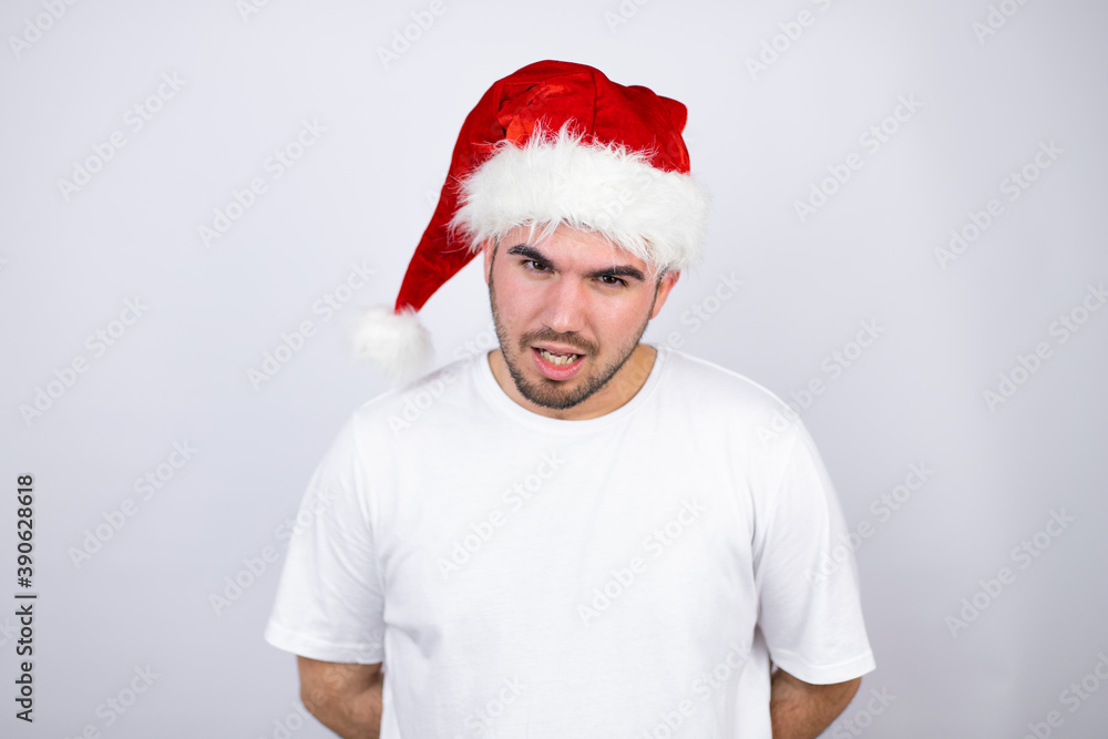 Young handsome man wearing a Santa hat over white background afraid and shocked with surprise and amazed expression, fear and excited face. Young handsome man wearing a Santa hat over white background afraid and shocked with surprise and amazed expression, fear and excited face.