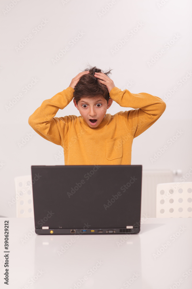 Vertical shot of a little boy looking shocked, standing in front of his laptop Vertical shot of a little boy looking shocked, standing in front of his laptop