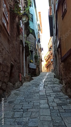 An ancient narrow street of an old European city. There is a very small distance between the colorful houses. The sidewalk is paved with large stone tiles. Laundry is dried on small balconies. © MartinsArts