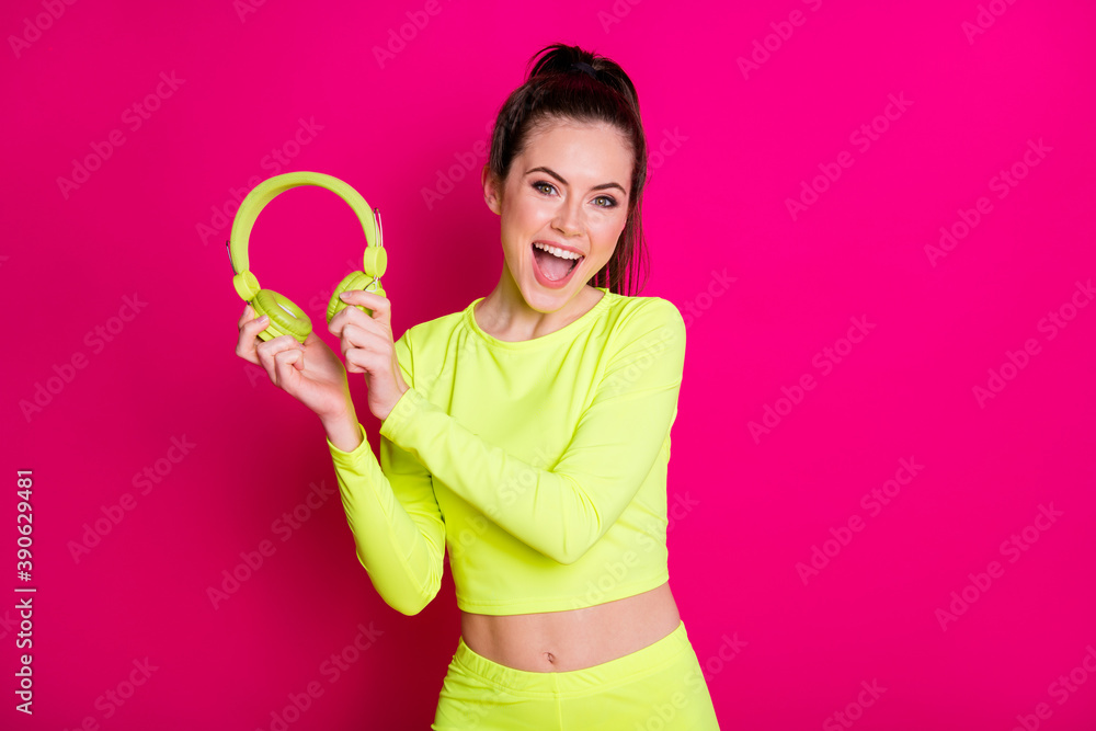 Portrait photo of happy sportswoman with ponytail keeping earphones wearing yellow sportswear isolated on vivid fuchsia color background Portrait photo of happy sportswoman with ponytail keeping earphones wearing yellow sportswear isolated on vivid fuchsia color background