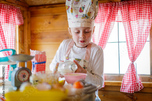Young girl in wendy house pouring milk  pretending to cook in kitchen