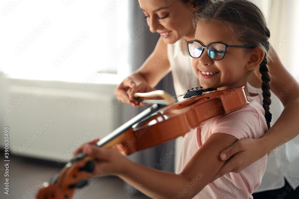 Young woman teaching little girl to play violin indoors Young woman teaching little girl to play violin indoors
