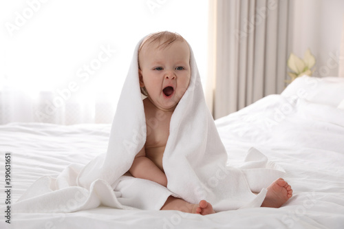 Cute little baby with soft towel on bed after bath