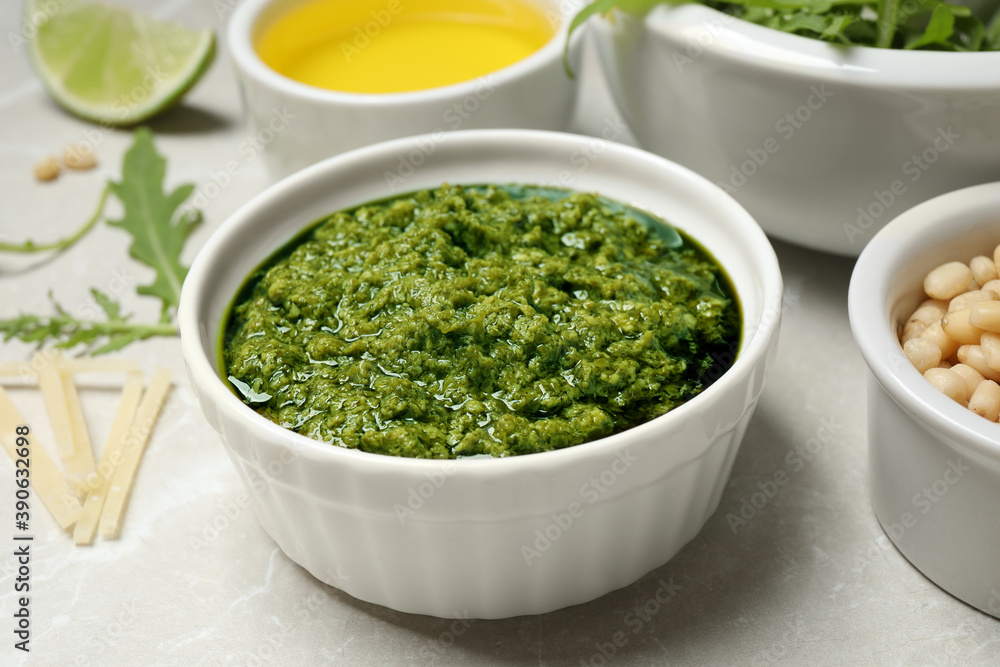 Bowl of tasty arugula pesto and ingredients on light table Bowl of tasty arugula pesto and ingredients on light table