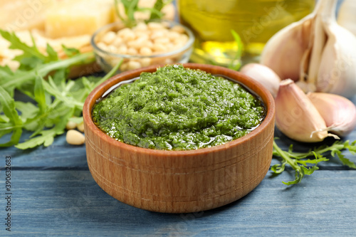 Bowl of tasty arugula pesto and ingredients on blue wooden table