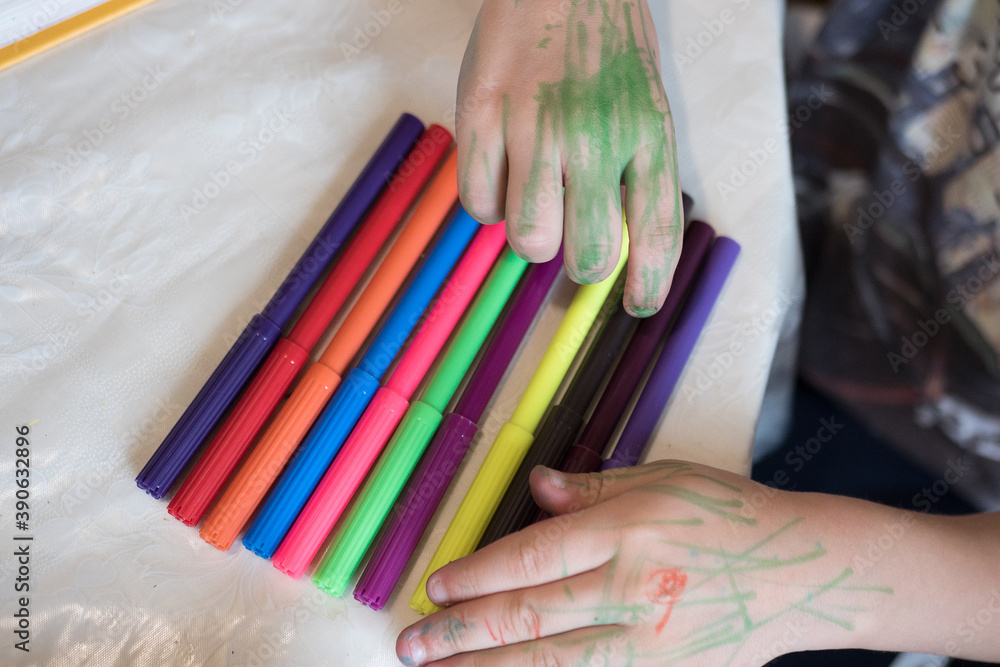 Fototapeta premium A boy, child holding different colorful pencils of different colors close up on white background..